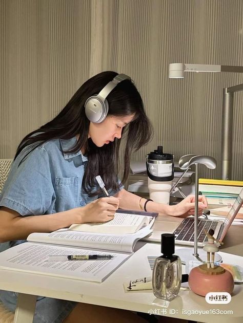 a woman sitting at a desk with headphones on writing in front of a laptop