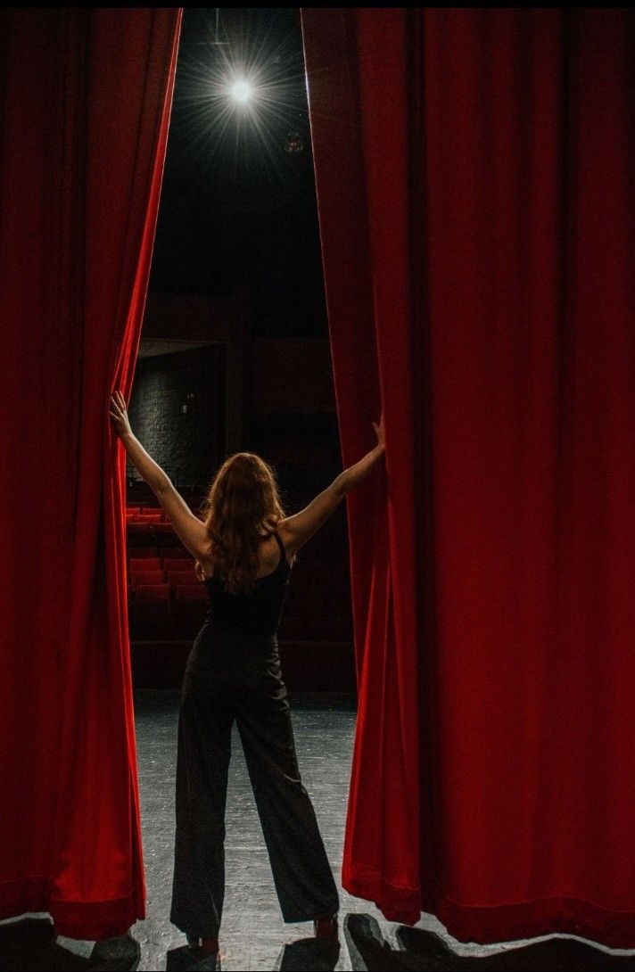 a woman standing in front of red curtains with her hands up and arms outstretched behind the curtain