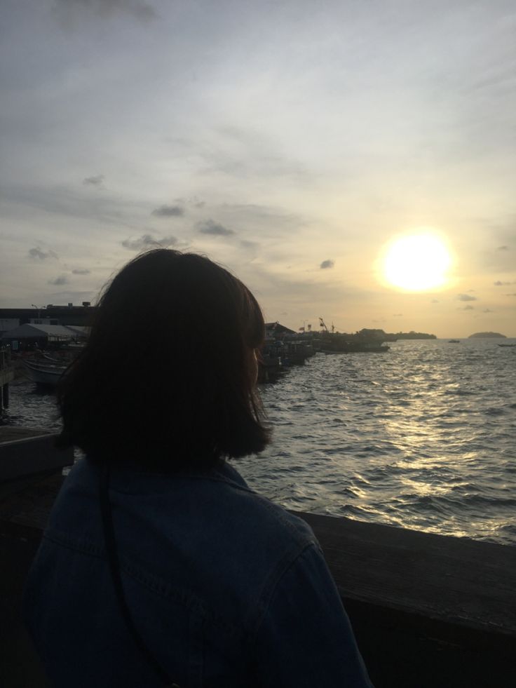 a woman is looking out over the water at sunset