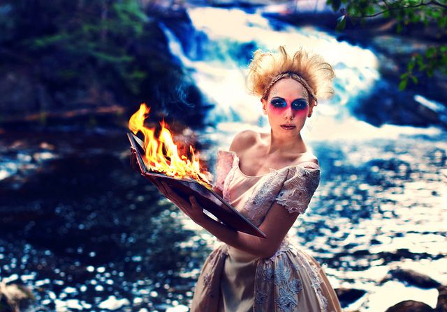 a woman holding a tray with flames in her hands near a river and waterfall wearing sunglasses