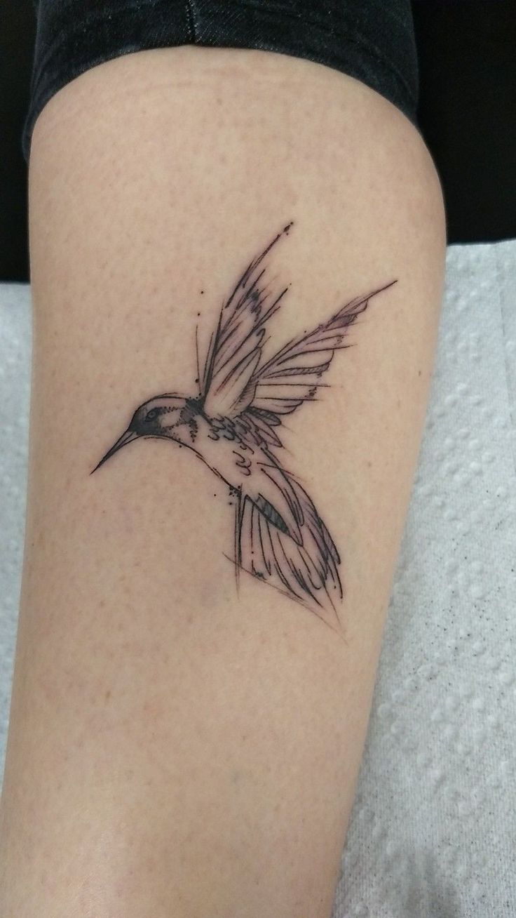 a small tattoo on the leg of a woman with a hummingbird flying above it