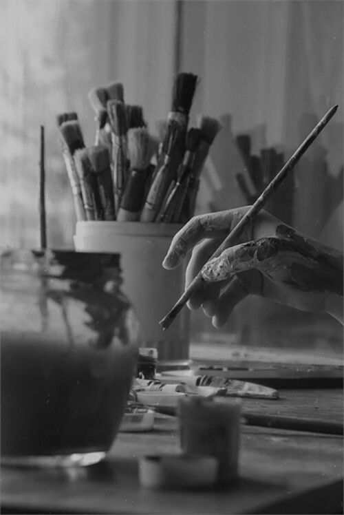 a black and white photo of someone's hand holding a paintbrush over an easel