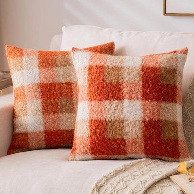 two orange and white checkered pillows on a couch with a blanket next to it