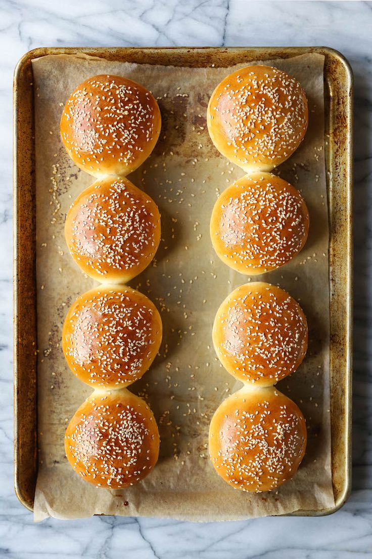 six buns on a baking sheet with sesame seeds sprinkled on top, ready to go into the oven