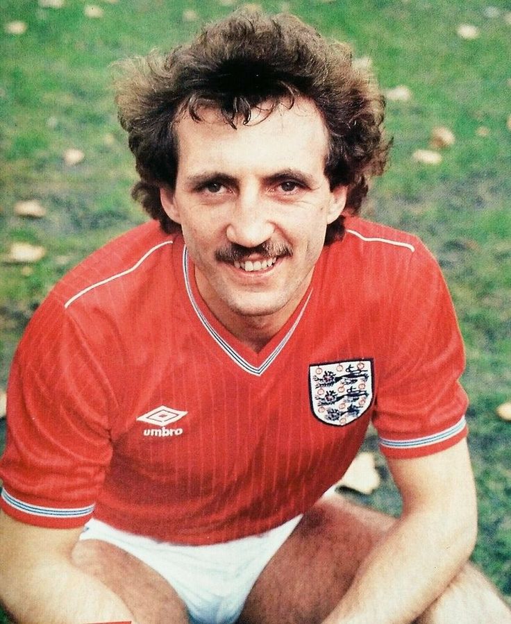 a man with a mustache sitting on the ground in a red shirt and white shorts