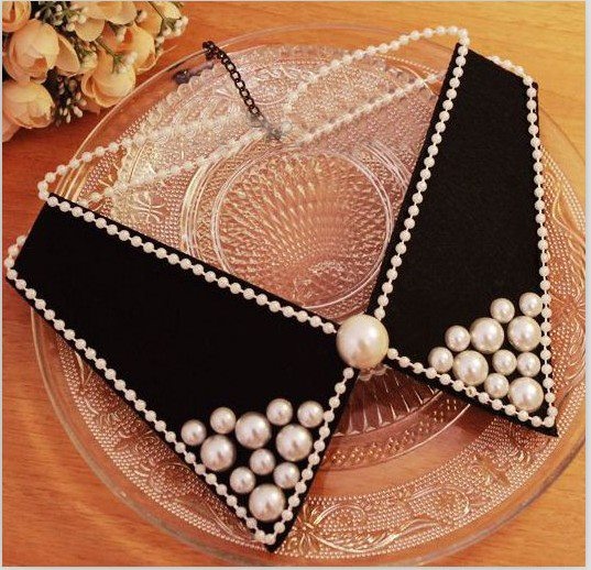 a black and white cake with pearls on it sitting on a glass plate next to flowers