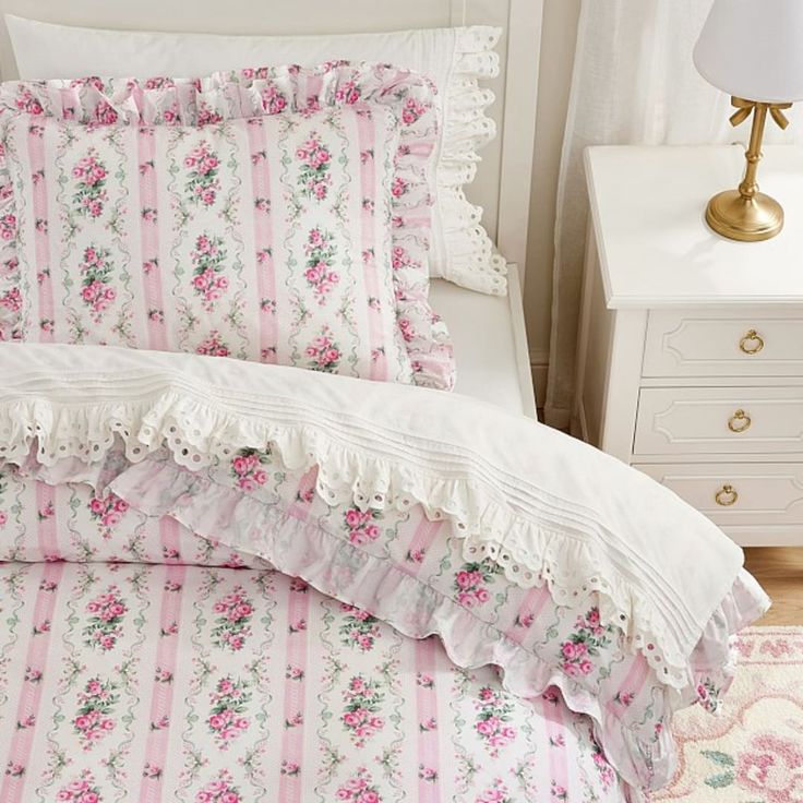 a bed with pink and white floral bedspread on top of it next to a night stand