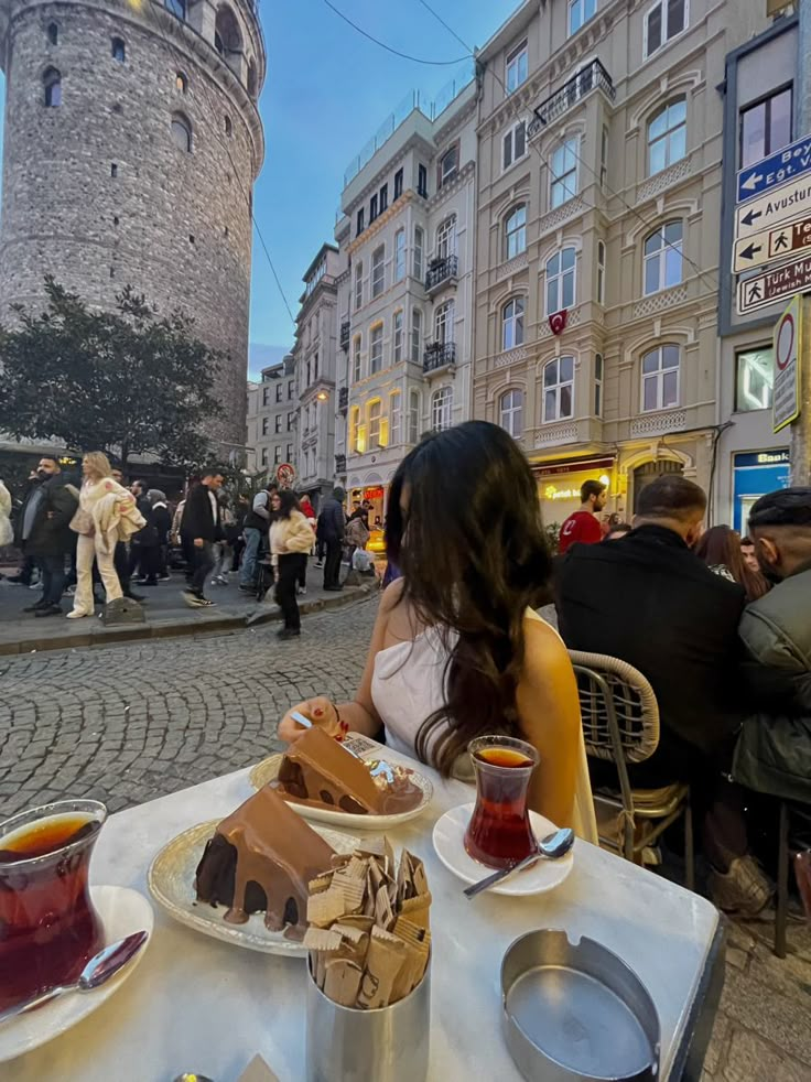 a woman sitting at a table with food in front of her and people walking by