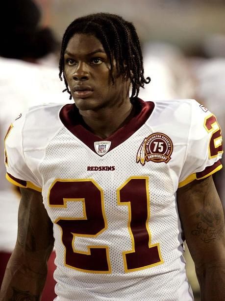 a man with dreadlocks standing on the sidelines wearing a football uniform and looking at the camera