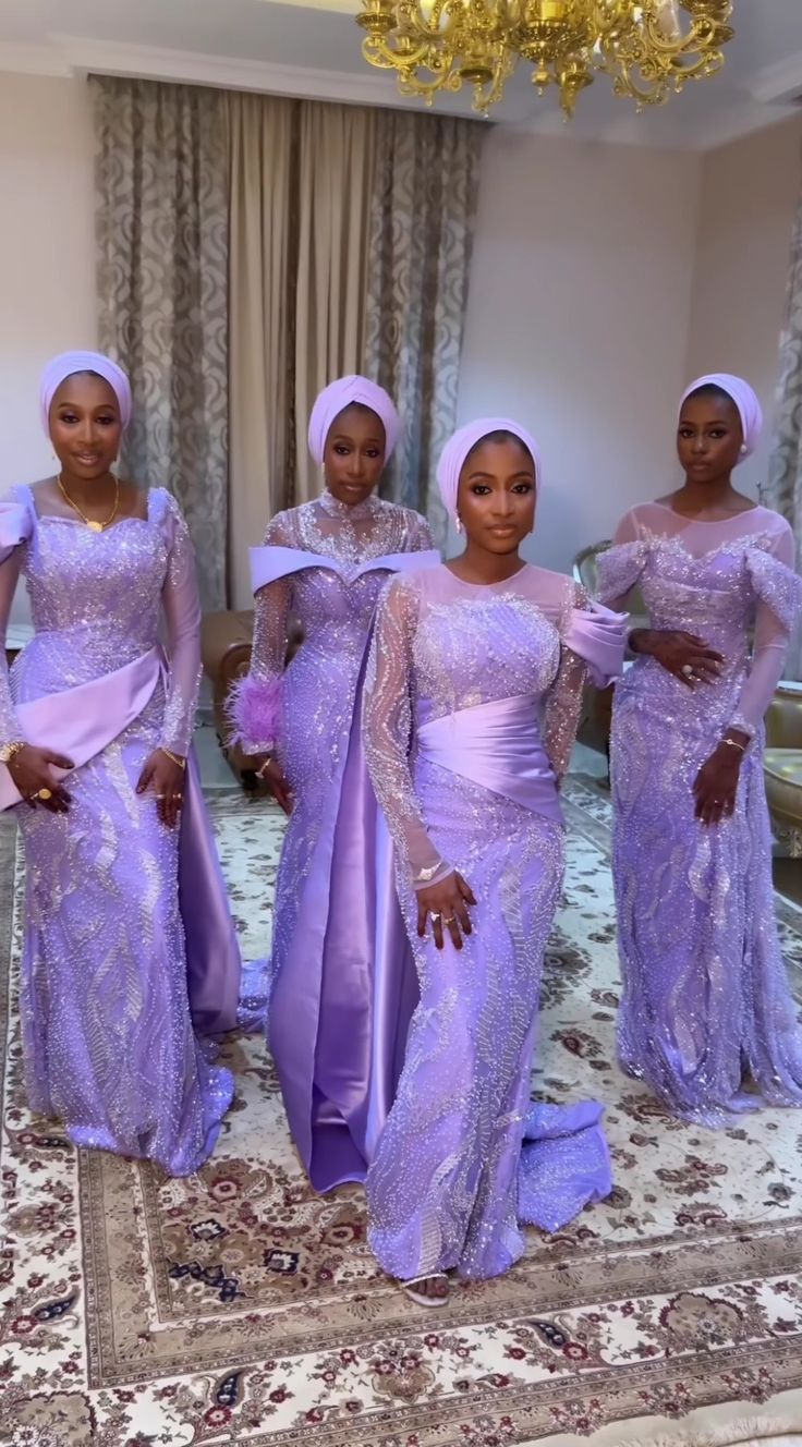 three women in purple dresses standing next to each other on a carpeted area with a chandelier hanging from the ceiling