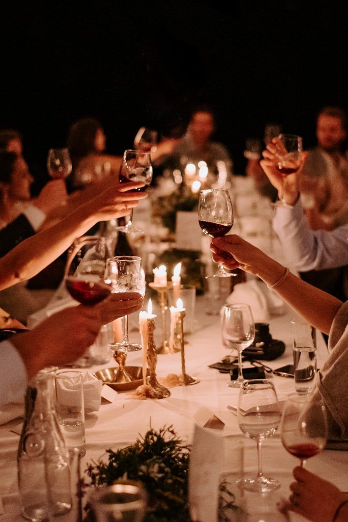 people are toasting wine glasses at a dinner table with candles and greenery on the table