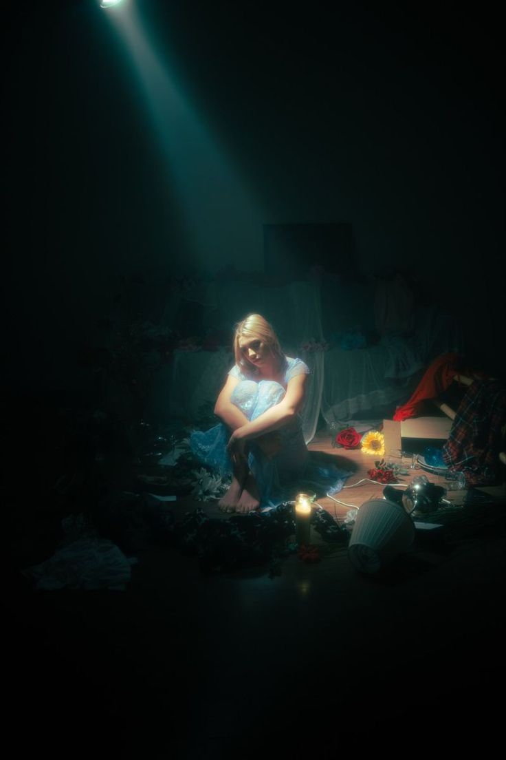 a woman sitting on the floor in front of a light that is shining down over her