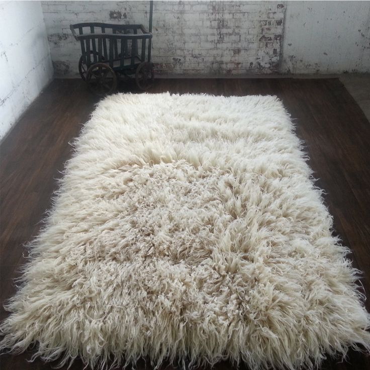 a white shaggy rug sitting on top of a wooden floor next to a brick wall