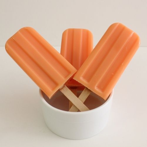 an orange popsicle sitting in a white cup filled with ice cream and caramel