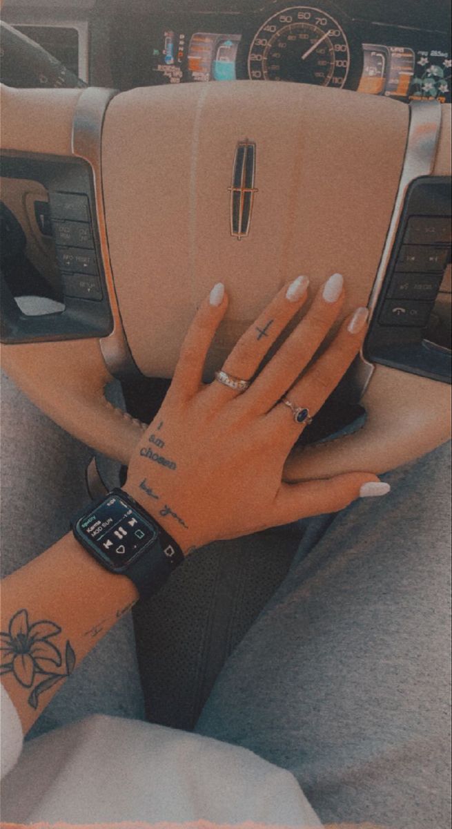 a woman's hand on the steering wheel of a car with her wrist tattoo