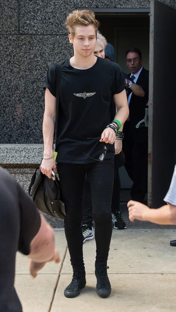 a man in black shirt and leggings walking on sidewalk with other people behind him