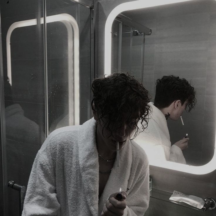 a woman is looking at her cell phone in the mirror while another man looks on