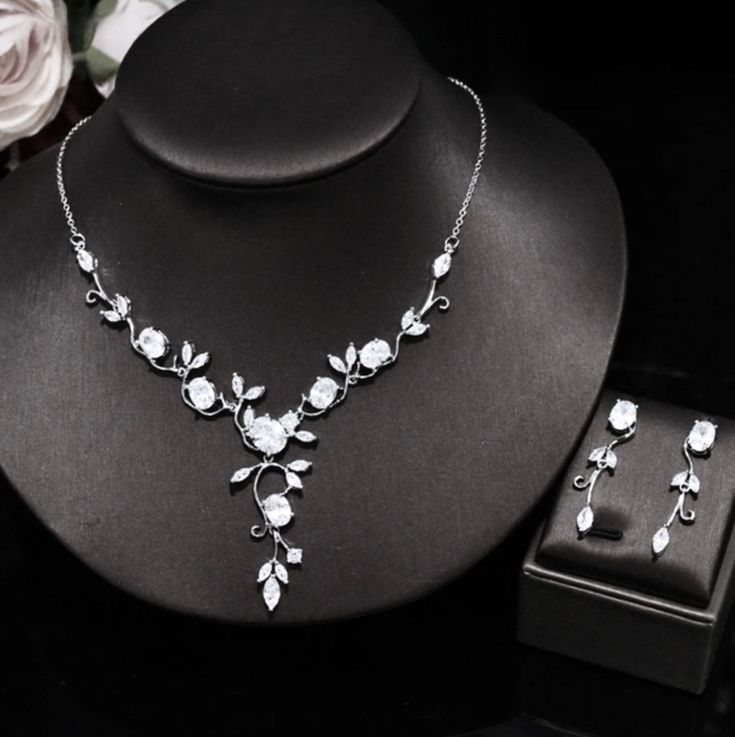 a necklace and earring set on a black display stand next to a white rose