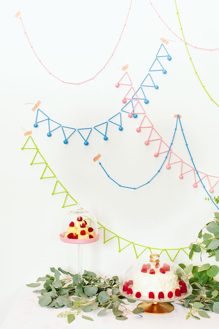 a cake on a table surrounded by greenery and other decorations, with a white wall in the background