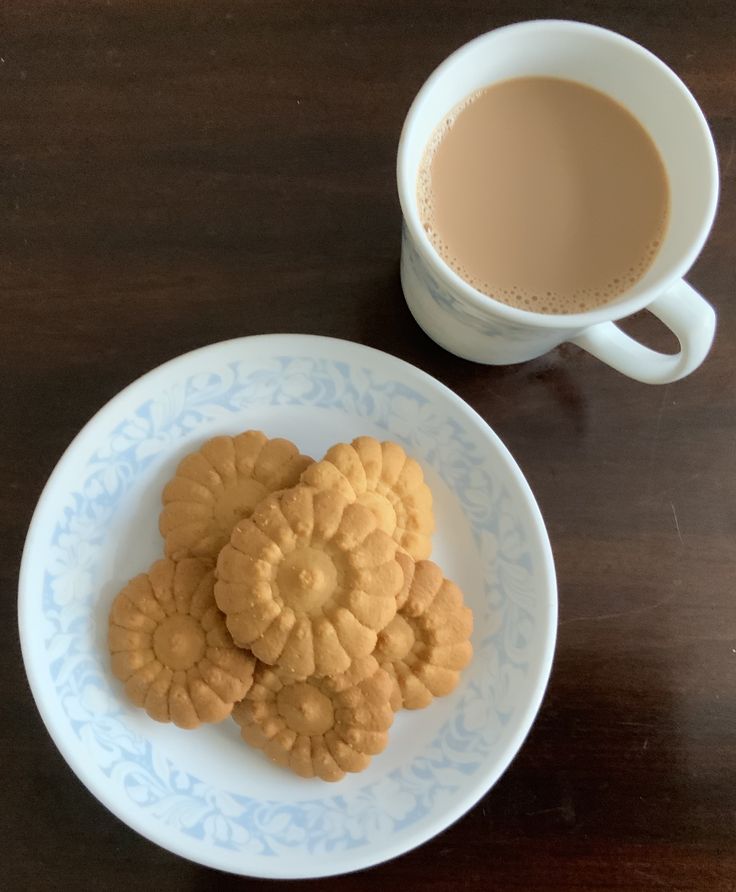 two cookies on a plate next to a cup of coffee and saucer with liquid in it