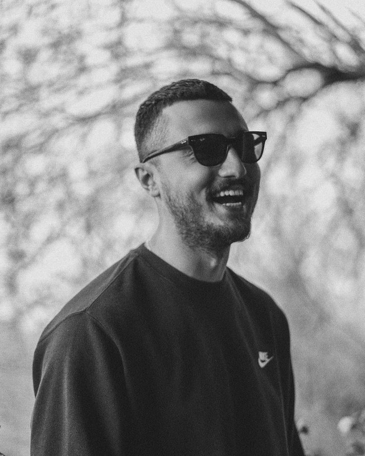 a man wearing sunglasses standing in front of a tree