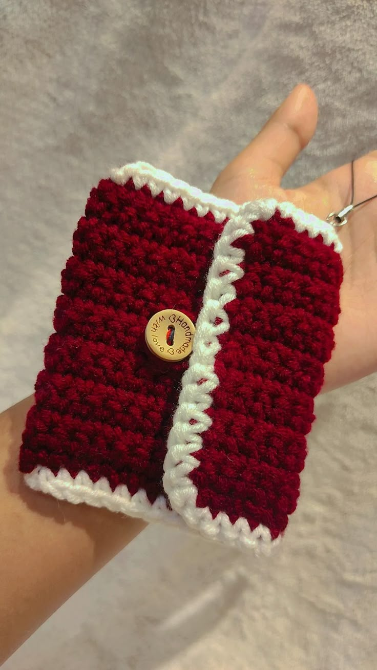 a hand holding a red and white crocheted wristlet with a button on it