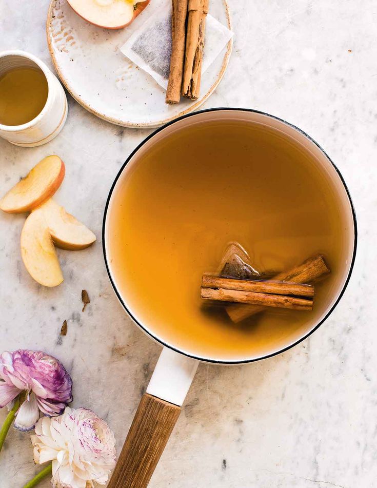 a cup of apple cider next to some cinnamon sticks and flowers on a table