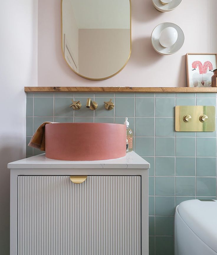 a bathroom with pink and blue tiles on the wall next to a white toilet, sink and mirror