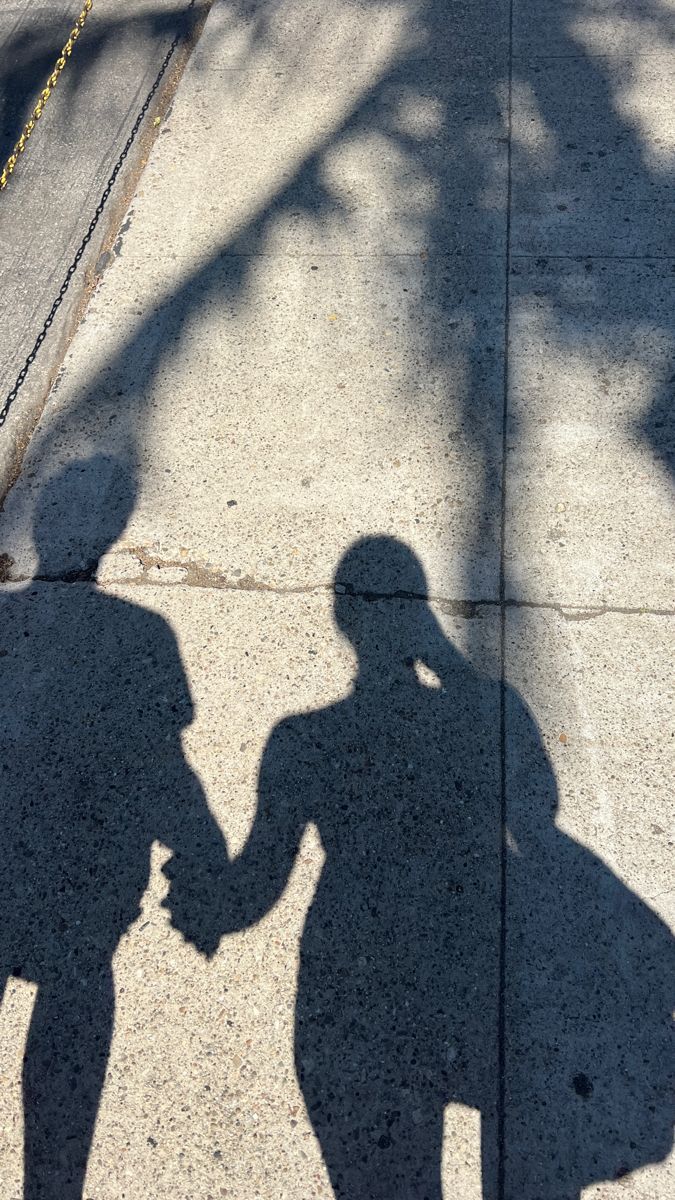 the shadow of two people holding hands while walking down the sidewalk on a sunny day