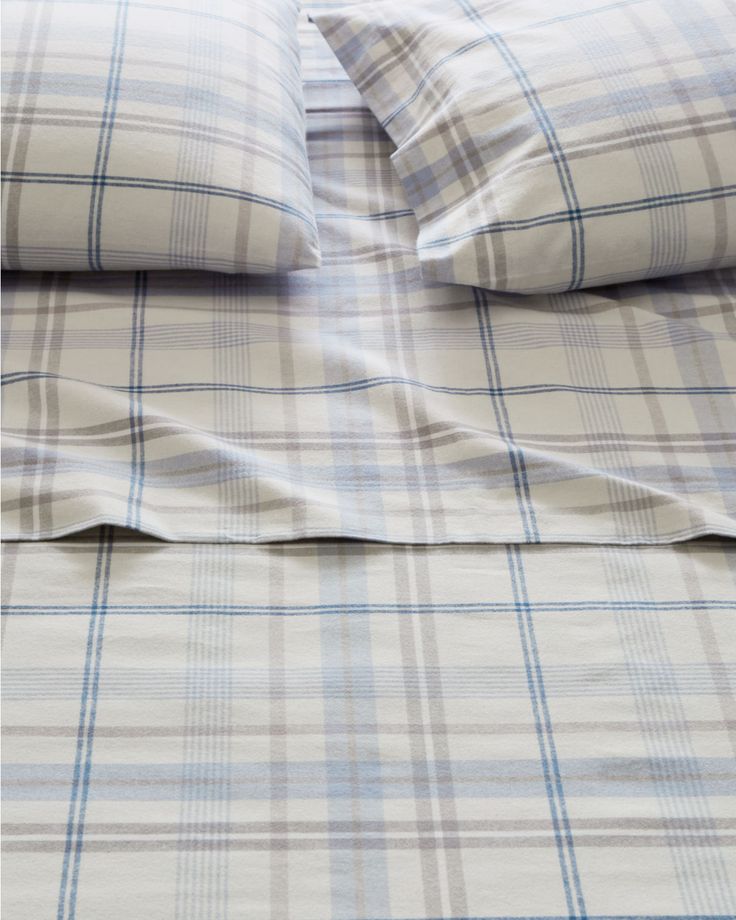 an unmade bed with blue and white plaid sheets