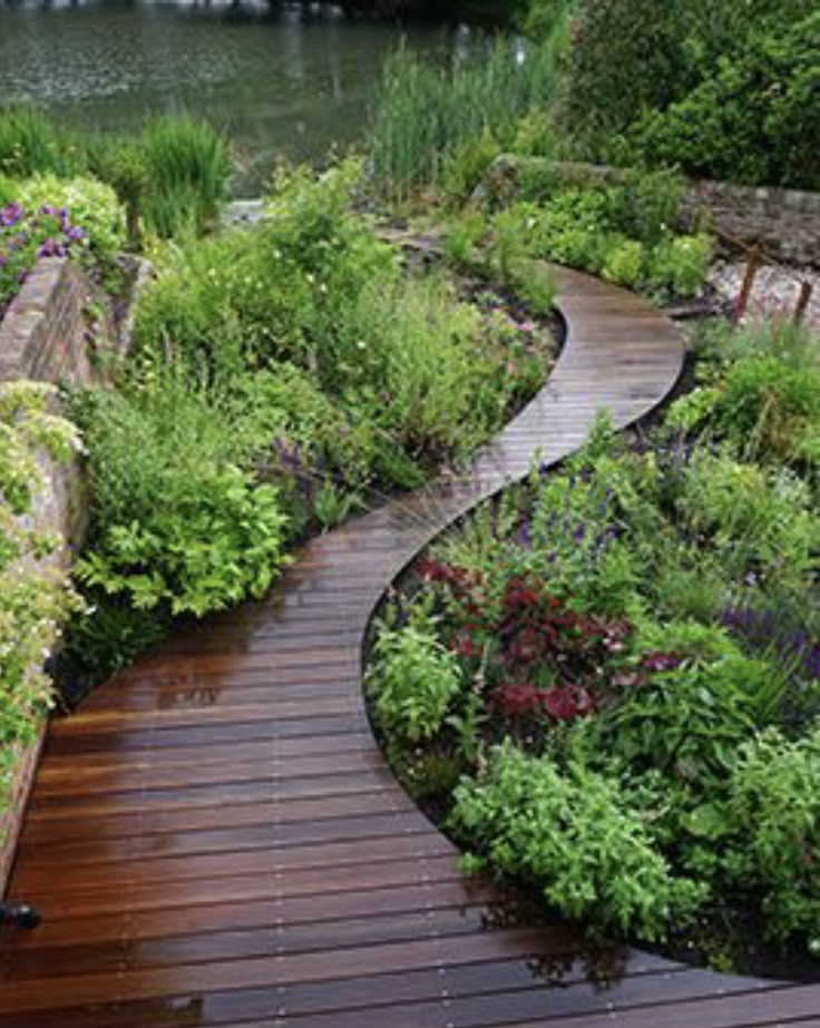 a wooden walkway surrounded by lots of flowers and greenery next to a body of water