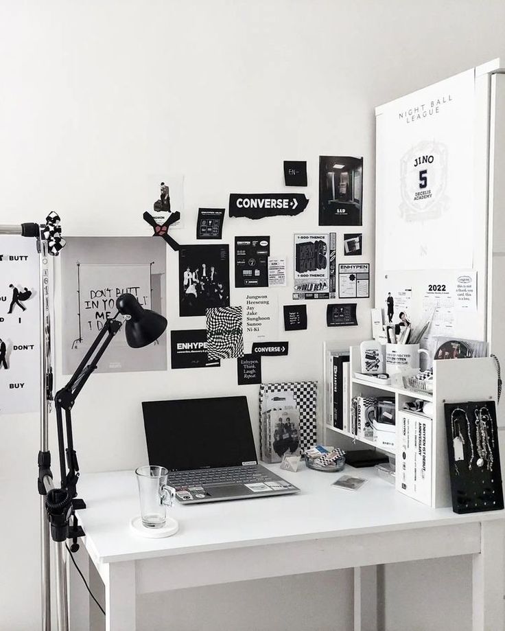 a white desk topped with a laptop computer next to a wall covered in black and white pictures