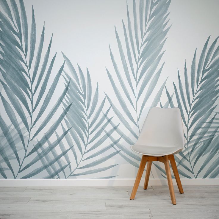 a white chair sitting in front of a wall with palm leaves painted on it's side