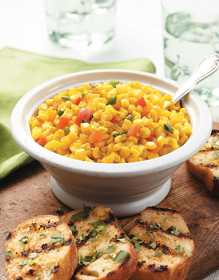 a white bowl filled with corn next to slices of bread