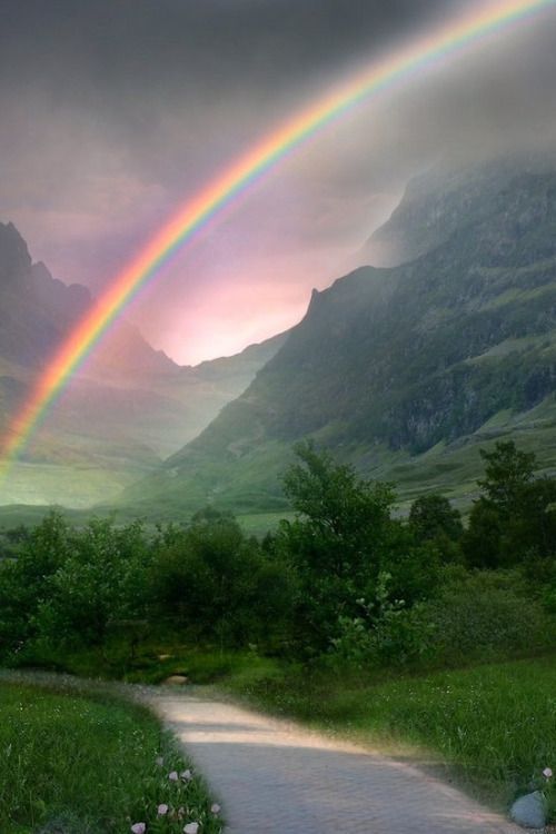 a rainbow shines brightly in the sky over a mountain valley and river as it rains