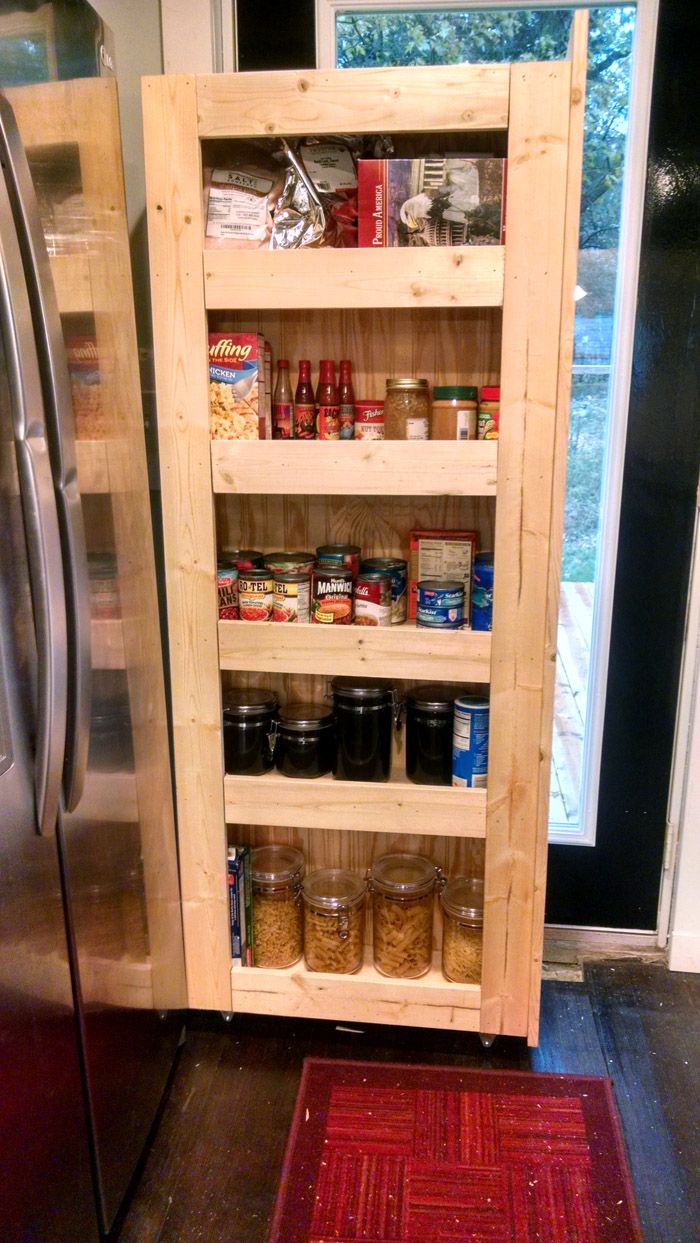 an open pantry door in a kitchen next to a stainless steel refrigerator and red rug