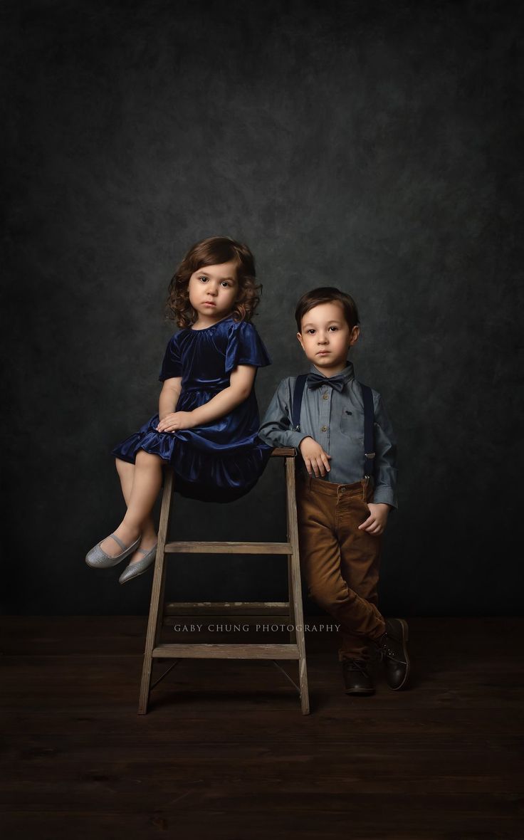 two children are sitting on a stool and posing for the camera