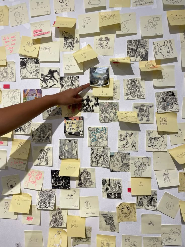 a person pointing at post - it notes on a wall covered in drawings and writing