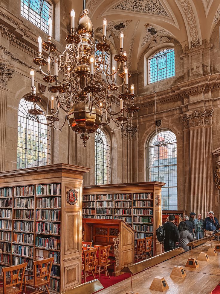 an old library with chandelier and tables full of books in front of large windows