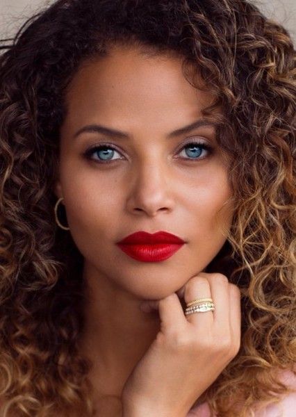 a close up of a person with curly hair and blue eyes wearing a red lipstick