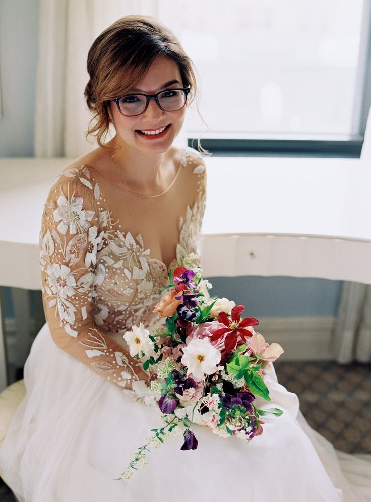 a woman sitting on a chair with a bouquet in her hand and smiling at the camera