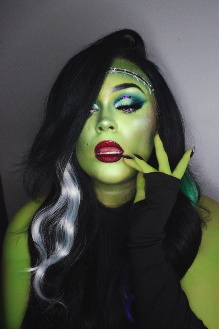 a woman with green makeup and black hair posing for the camera while holding her hand up to her face