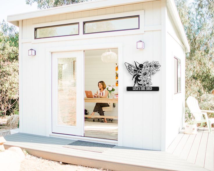 a woman sitting at a table in front of a small white building with glass doors