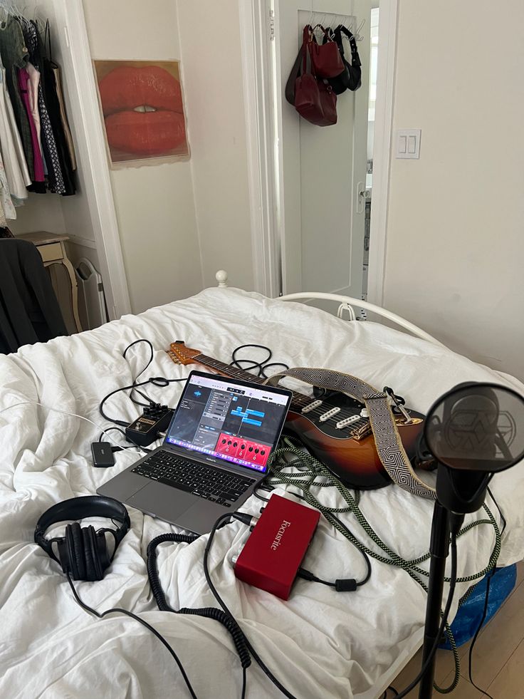 an open laptop computer sitting on top of a bed next to headphones and other electronics