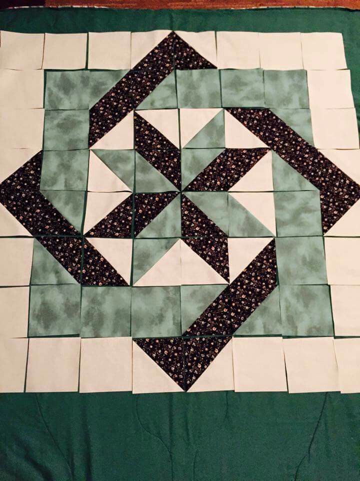 a quilted table topper with black and white designs on green fabric, sitting on a wooden surface