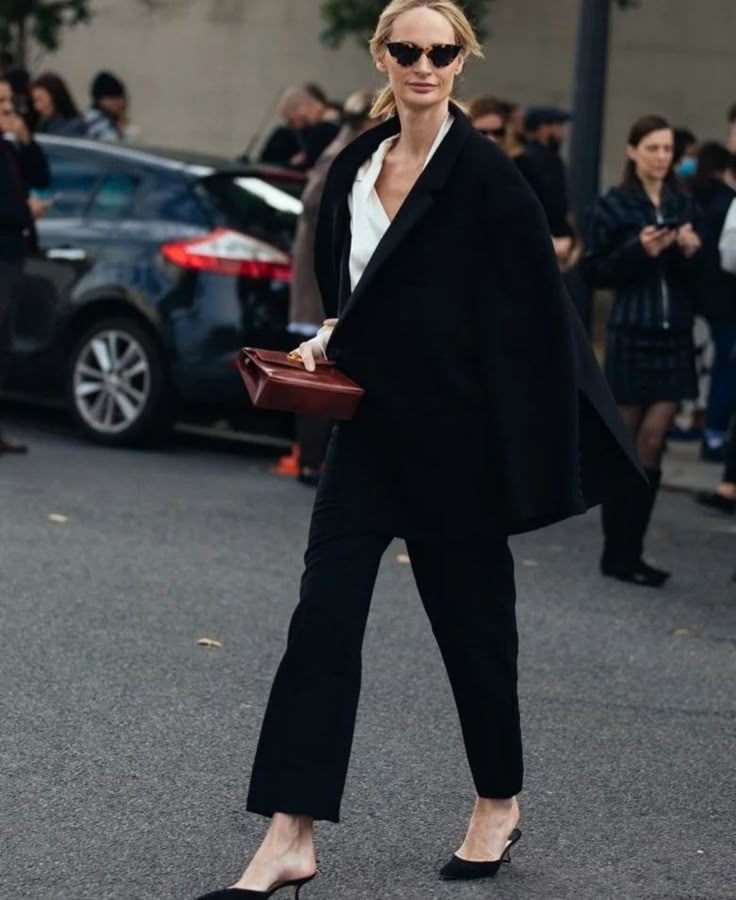 a woman in black and white is walking down the street with her hand on her purse