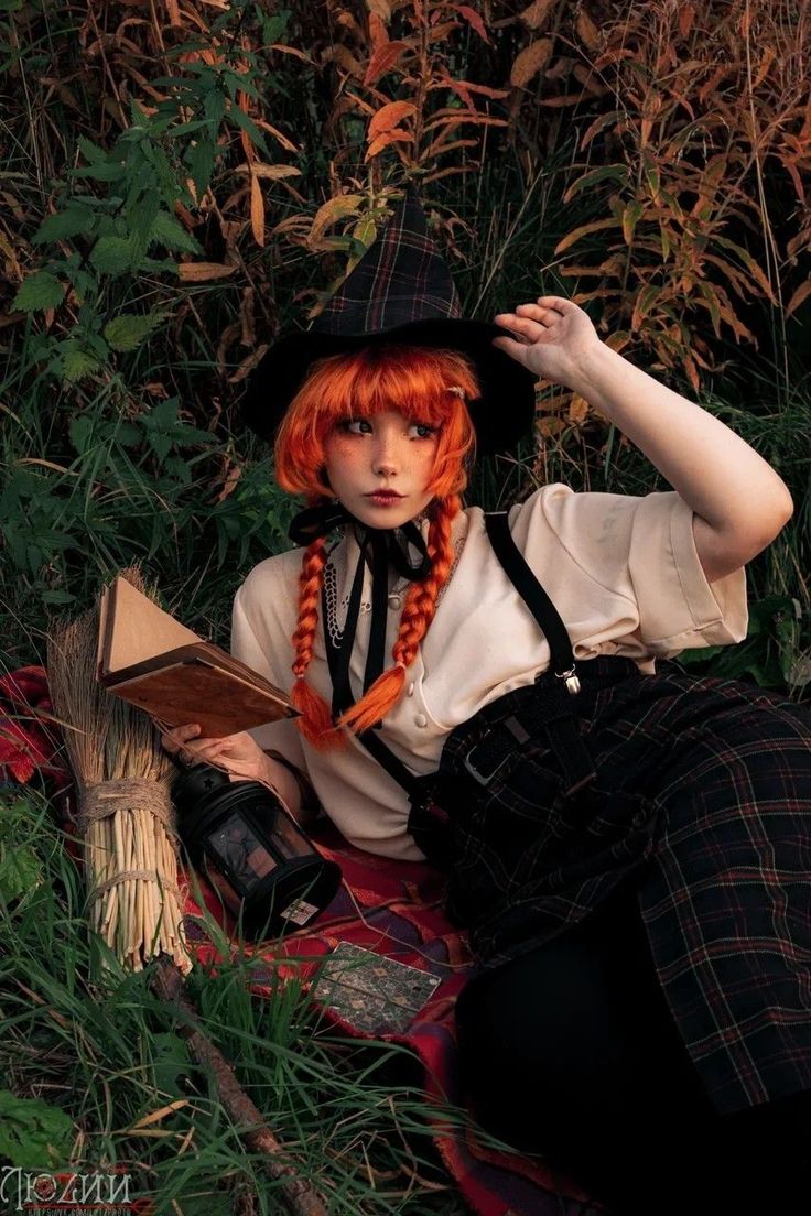 a woman with red hair sitting on the ground wearing a hat and holding a book