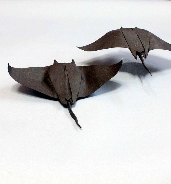 two brown origami bats sitting on top of a white table next to each other