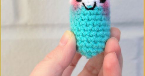 a hand holding a small crocheted llama with black eyes and pink cheeks