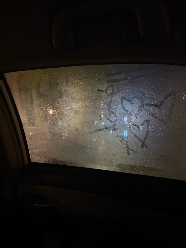 the window is covered with graffiti and raindrops in the dark, as seen from inside a car